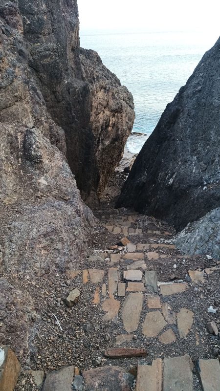 Un reste d'escalier qui descend entre 2 roches noirs